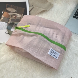 Pink checkered travel organizer bag with bright green zipper on white faux fur background