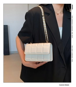 Close-up of beige quilted crossbody bag with gold-tone chain strap on black blazer