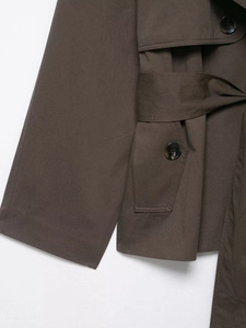 Detail eines dunkelbraunen Trenchcoats mit Gürtel, Marmorknöpfen und Twill-Stoffstruktur