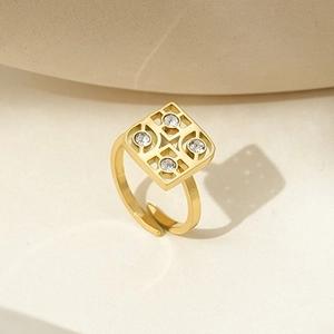 Macro shot of gold square hollow ring featuring four zircons on beige stone