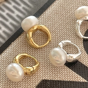 Detailed view of gold and silver pearl hoop earrings on a textured woven background