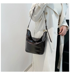 Detailed side view of a glossy dark brown leather hobo bag on a trench coat model