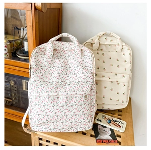 Detail of two floral print backpacks in beige and pink on vintage wooden furniture