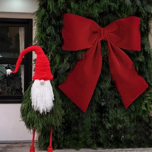 Large red velvet Christmas bow with a bearded gnome ornament on green foliage background