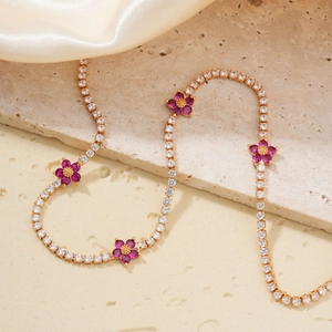 Detail of gold tennis chain with pink flower charms on satin and rock background