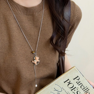 Close-up of wooden rocking horse pendant with silver plating and pearl on long chain