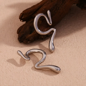 Detail of silver liquid metal ear cuff with abstract curved design on wooden texture