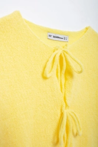 Close-up of yellow knit cardigan collar with tie-up detail and textile brand label