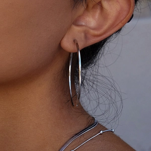 Close-up of a model wearing large silver stainless steel hoop earrings and a bead necklace