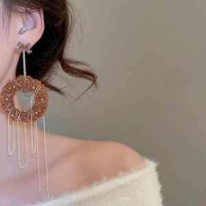 Detail of plush brown round earrings with delicate silver fringe chains on model