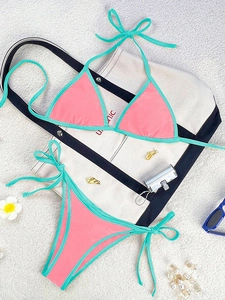 Flat lay of pink bikini set with mint green trim and beach accessories on light surface