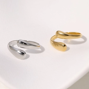 Detailed close-up of gold and silver teardrop open rings on a beige background