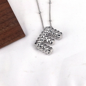 Macro shot of silver letter E necklace pendant with textured diamond pattern finish