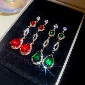 Close-up of elegant gold drop earrings with red and green gems on black velvet