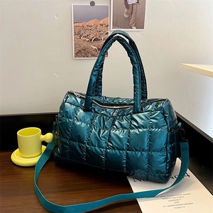 Detail of teal metallic quilted puffer bag on a dark wood surface with soft lighting