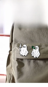 Detail of cute ghost enamel pins with dagger and bottle on dark green canvas backpack