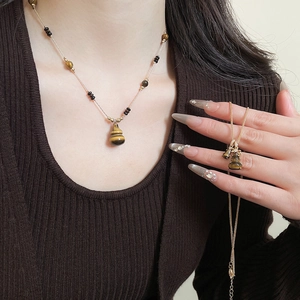 Close-up of a tiger eye gourd pendant necklace on a model wearing brown knitwear
