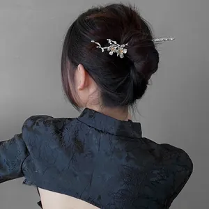 Detailed view of a silver plum blossom hair stick with gold accents on a model in qipao