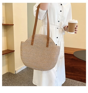 Detail of the woven straw tote bag with brown leather handles on a model shoulder