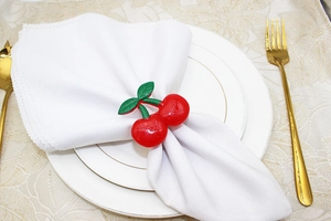 Detailed close-up of vibrant red cherry napkin ring with green leaves on white linen