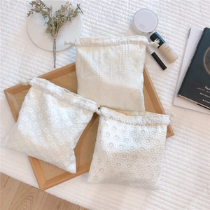Flat lay of white lace drawstring bags with intricate embroidery in a wooden tray