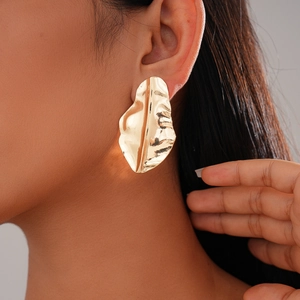 Close-up of irregular gold leaf earrings with pleated texture worn on model's ear