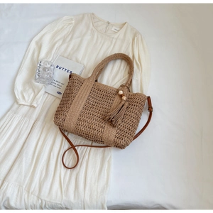 Flat lay of khaki straw woven tote bag with leather strap and tassel decorative ball