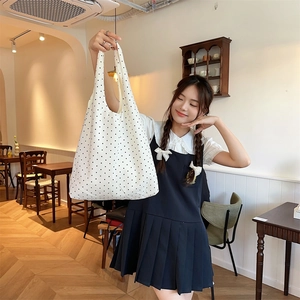 Detailed texture of white canvas tote with black polka dots shown in a bright cafe setting