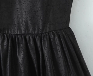 Détail macro de la robe en similicuir noir avec texture craquelée et taille plissée élégante