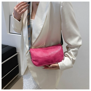 Detail of rose red baguette bag featuring a textured finish and patterned wide strap