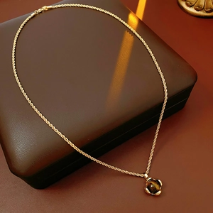 Detailansicht des Tigerauge-Anhängers an einer goldenen Kordelkette auf Leder