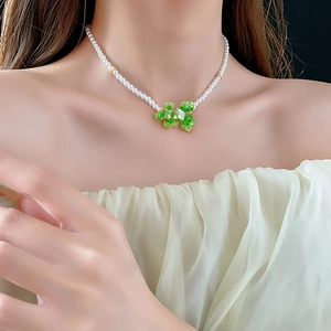 Detail of pearl necklace featuring a green clover pendant with gold plating on a model