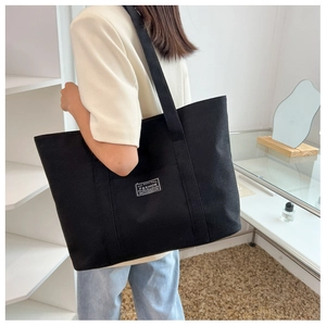 Canvas tote bag in black featuring fine fabric texture and label shown on model shoulder