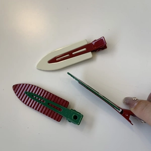 Detail of three metal hair clips in cream, dark red, and green with spring mechanism