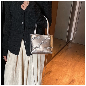 Detail of silver metallic handbag featuring decorative bows and a stylish metal chain strap