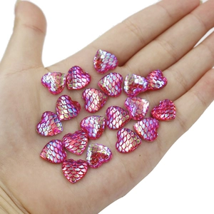 Close-up of pink heart-shaped resin cabochons with fish scale texture held in palm