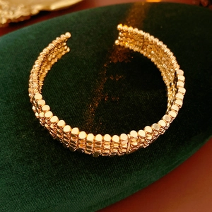Détail d'un bracelet manchette doré multicouche en perles sur velours vert foncé luxe