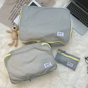Three-piece light grey travel organizer set with yellow zippers on white plush background