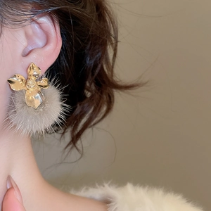 Close-up of elegant gold flower earrings with soft grey plush pompom on a model