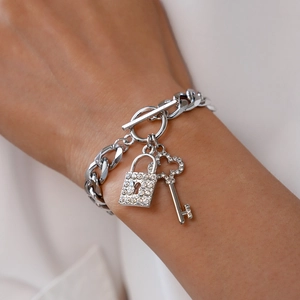 Detail view of silver Cuban chain bracelet featuring diamond-set lock and key charms