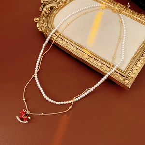 Close-up of red enamel rocking horse pendant on layered pearl necklace and gold chain
