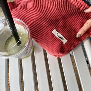 Close-up of red corduroy makeup bag texture with brand label on a white metal bench