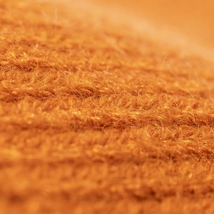 Close-up of knit texture on warm orange winter beanie hat showing soft wool fibers