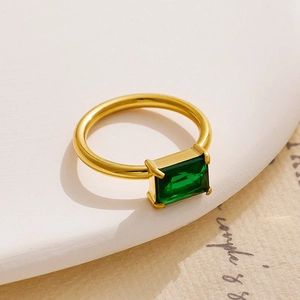 Close-up of 18K gold plated ring with emerald-cut green cubic zirconia on vintage paper