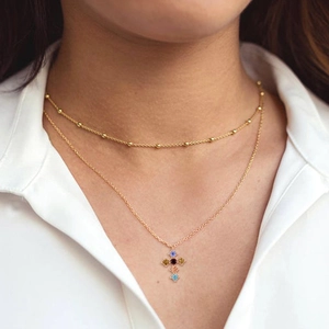 Collana a doppio strato dorata con ciondolo a croce in zircone colorato su camicia bianca