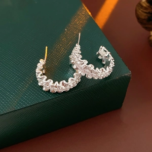 Macro shot of silver C-shaped earrings with wavy texture and zircon stones on green box