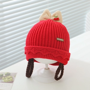 Détail du bonnet tricoté rouge pour bébé avec tresses, nœuds cerise et protège-oreilles