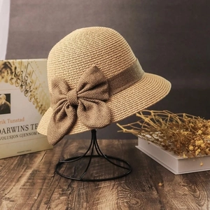 Detail of khaki straw hat with brown ribbon bow displayed on a minimalist stand