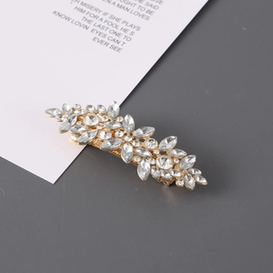 Detail view of a leaf-shaped gold hair clip with sparkling rhinestones on a white card