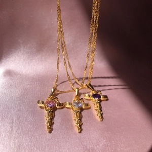 Golden snake cross necklaces with pink, clear and purple heart gems on pink satin fabric